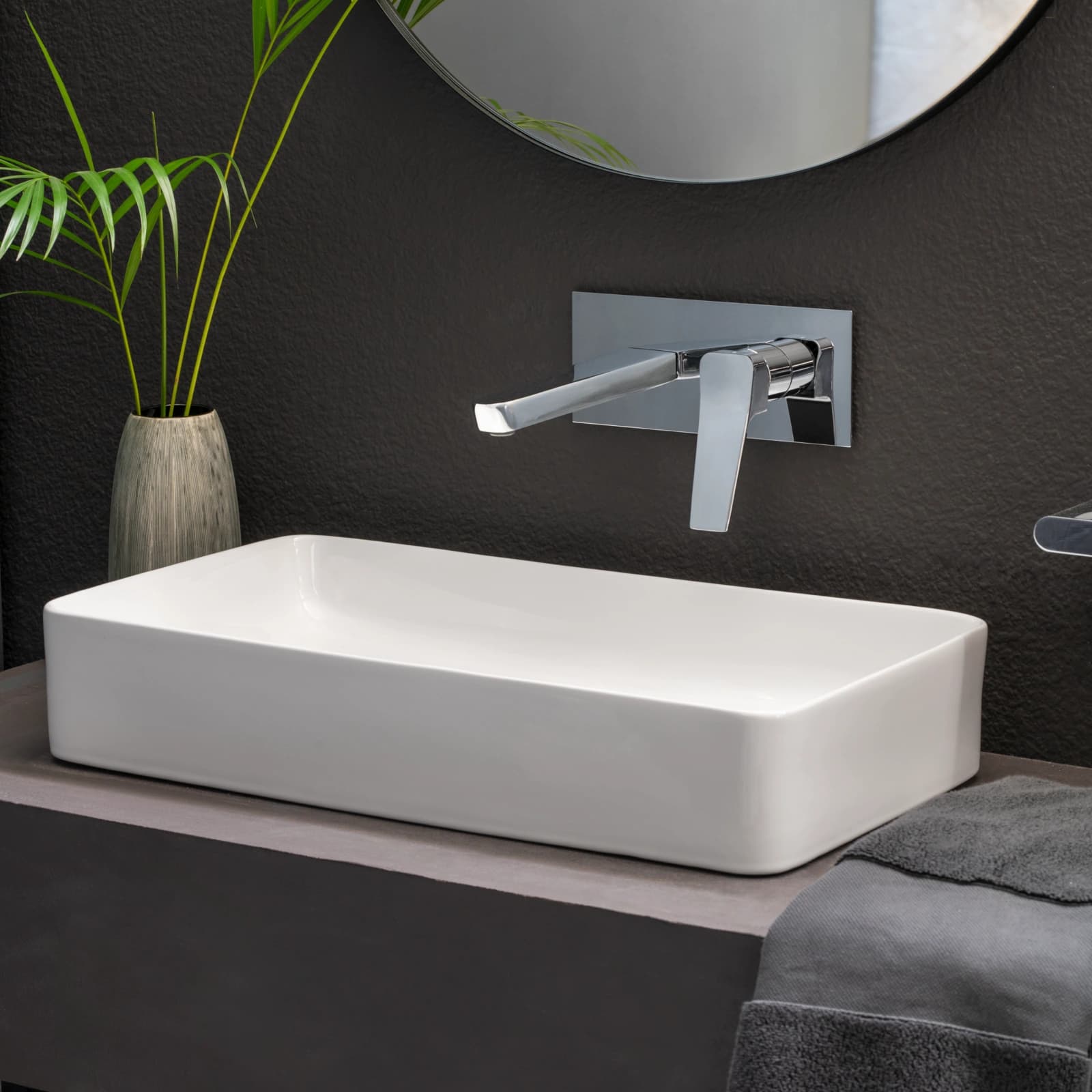 Aixeta de lavabo mural cromada ramonsoler sobre un lavabo blanc rectangular i una paret fosca