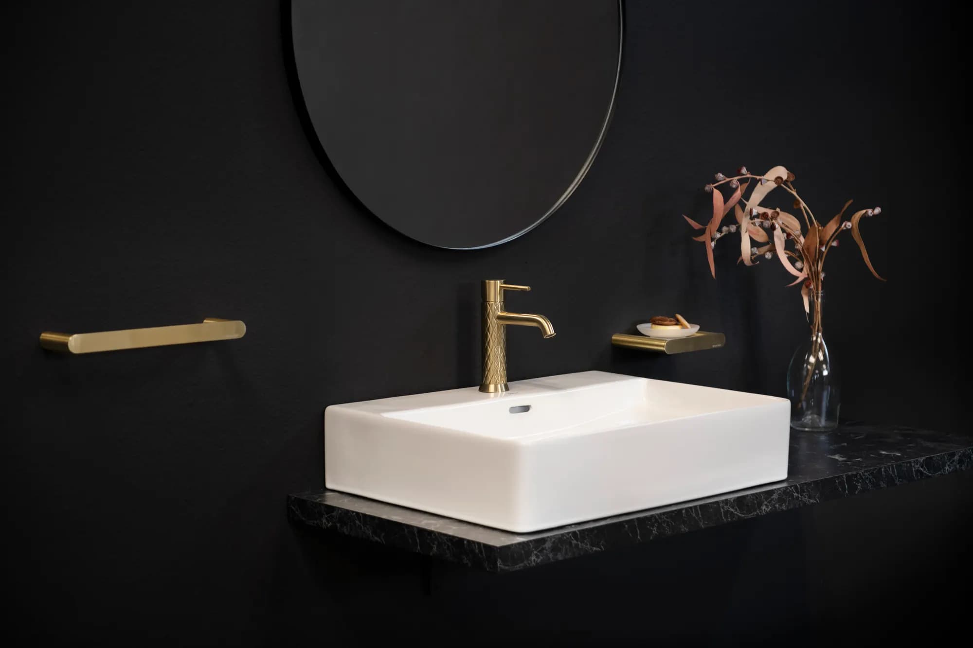 Bad mit schwarzer Wand, rundem Spiegel, weißem Waschtisch und ramonsoler Armatur in Gold