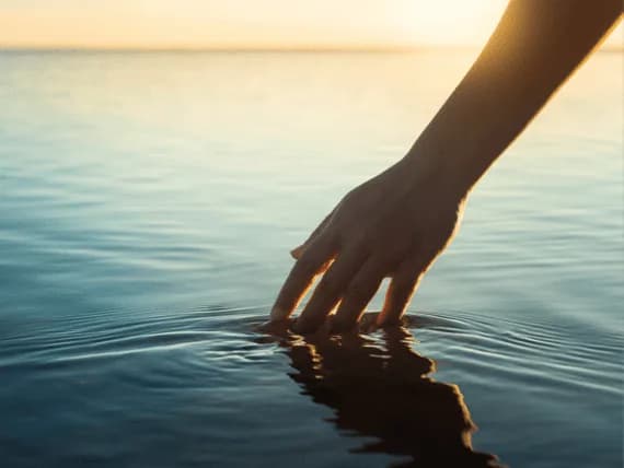 Mano rozando la superficie del agua al atardecer