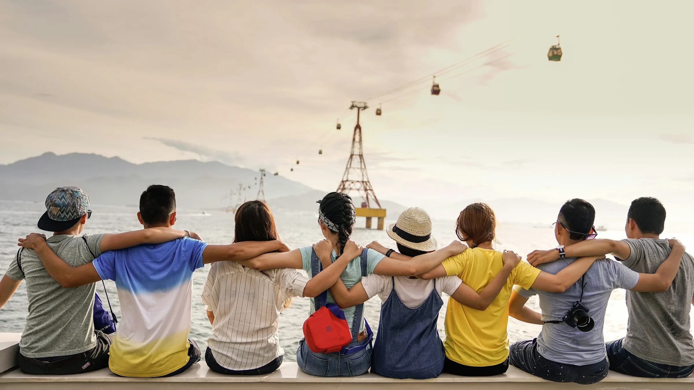 Group of people sitting with their backs to the camera, arms around each other, facing the sea